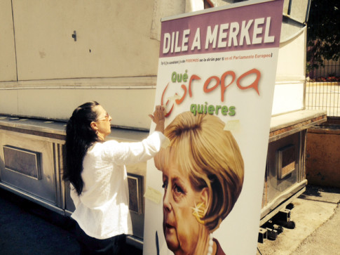 Una persona coloca una pegatina en el cartelón de Merkel (Foto cortesía de Podemos Rivas)